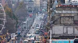 A busy urban street with historic buildings, including a prominent tower and the Royal British Hotel.