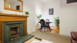 A living room with a fireplace, a dining table with chairs, and a large mirror on the wall.