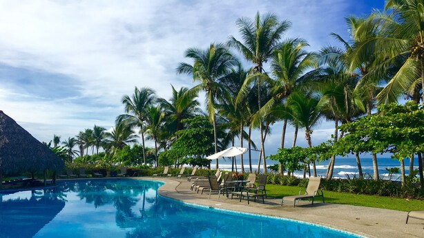 Una piscina circondata da palme e da una struttura con tetto di paglia, con vista sull'oceano.