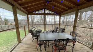 A covered outdoor patio with a wooden deck, metal table and chairs, and string lights. - SUPER UPSCALE RANCH! (Mentor)