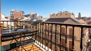 A balcony with a table and chairs, overlooking a cityscape with historic buildings and a clear blue sky.