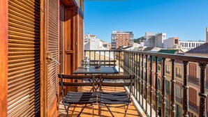 A balcony with a table and two chairs, overlooking a cityscape with buildings.