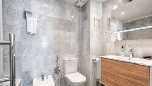 A modern bathroom with a marble wall, a wooden vanity, a toilet, and a bidet.