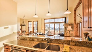 A kitchen with granite countertops, stainless steel sinks, wooden cabinets, pendant lighting, and large windows offering views of the outdoors. - Crested Butte Townhome w/ Views - Steps to Lifts! (Mt. Crested Butte)