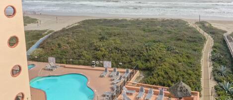 Una piscina en la azotea con sillones de descanso, un paraguas de paja y vista a la playa y al océano.