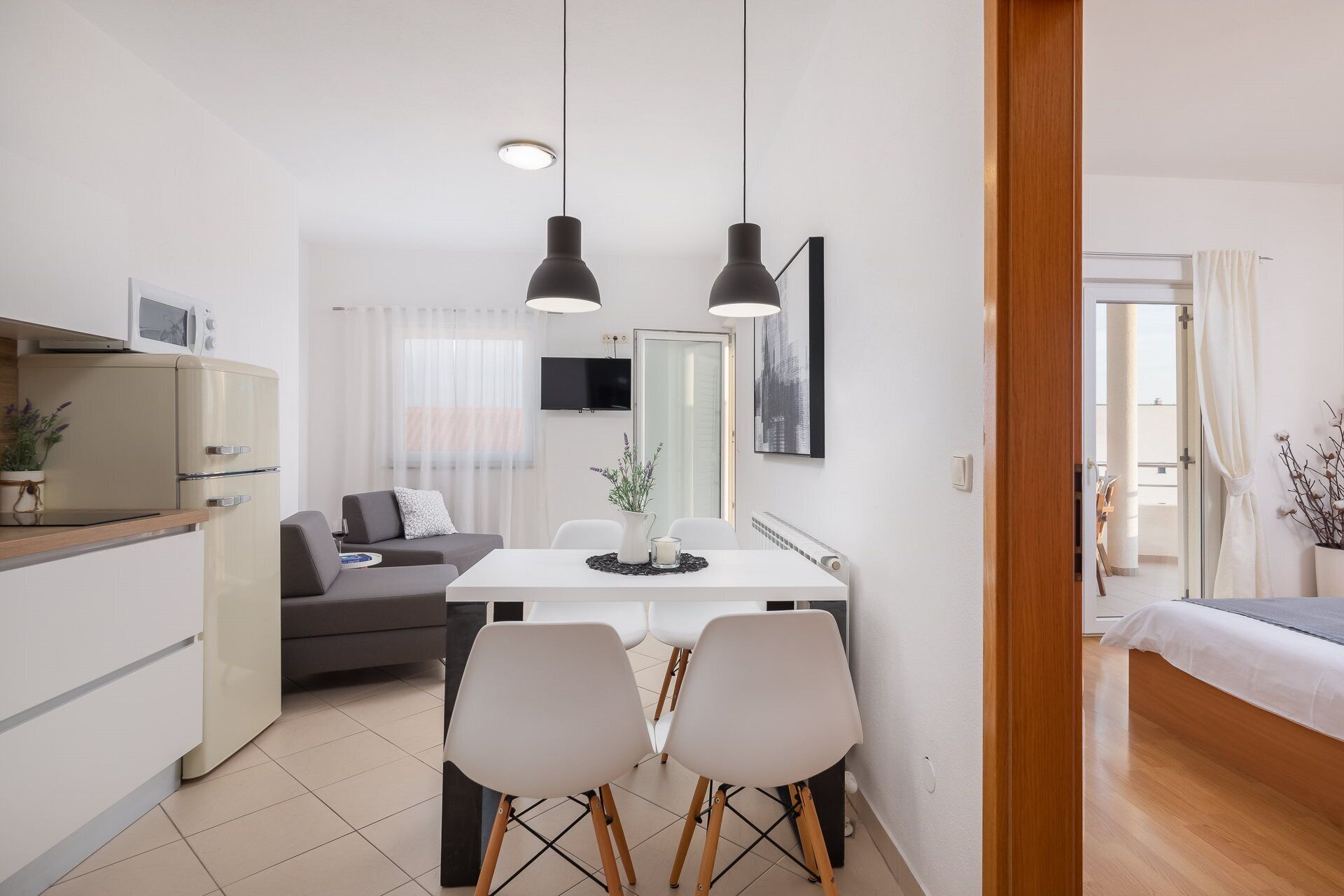 A modern, well-lit living space with a dining area, a sofa, a TV, and a bed.