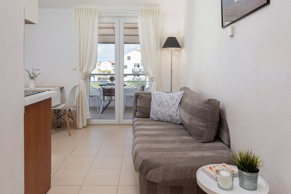 A cozy living area with a sofa, a small table with a plant, and a view through a glass door to an outdoor balcony.