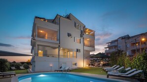 A multi-story building with a swimming pool, lounge chairs, and a well-lit balcony area. - Apartments Arausa with Pool (Vodice)