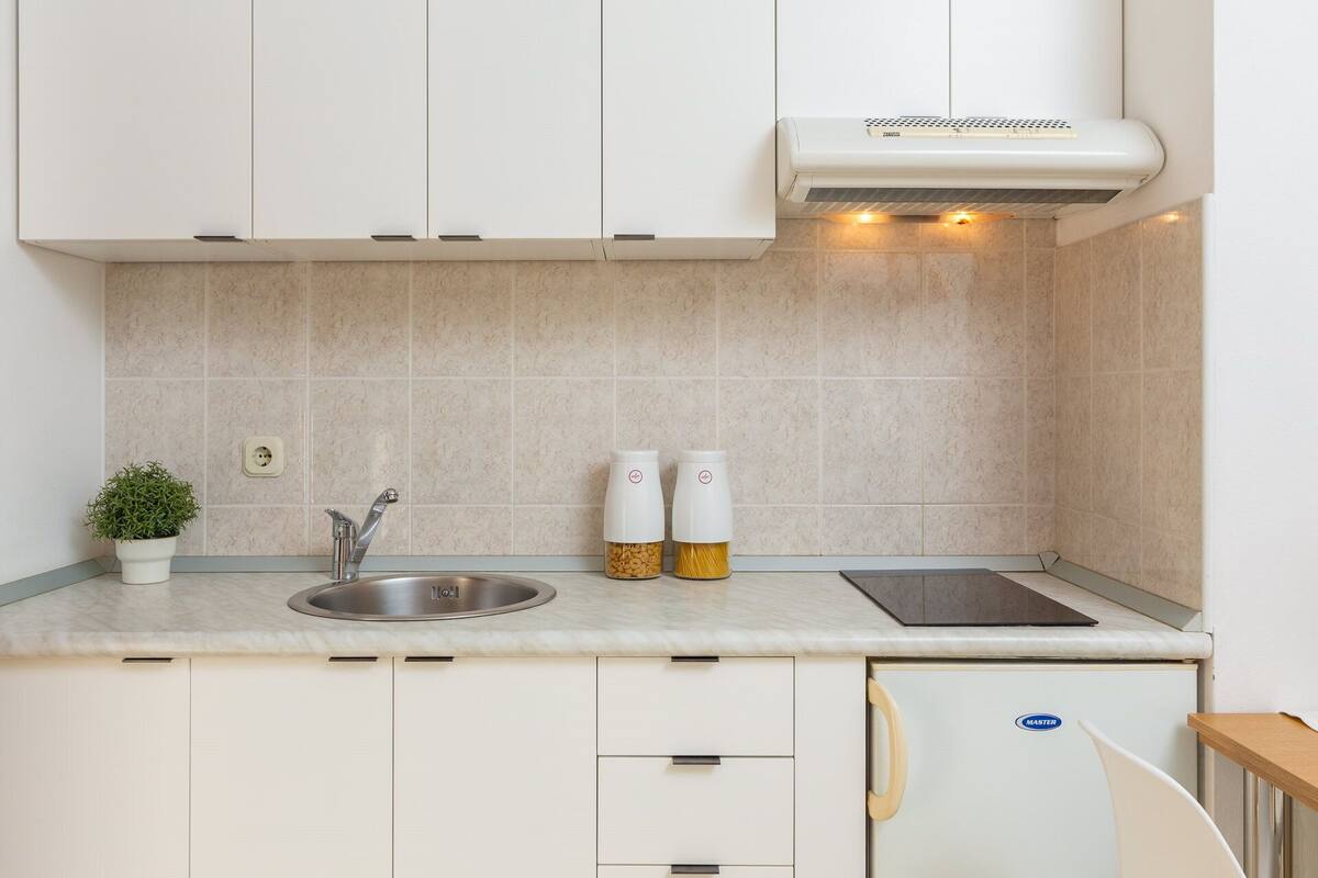 A modern kitchen with white cabinets, a stainless steel sink, a built-in stove, and a small refrigerator.