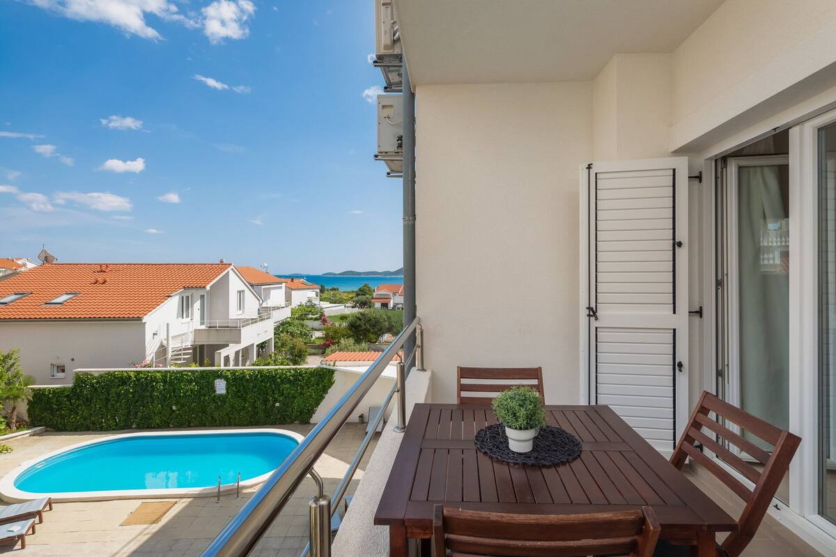 A balcony with a wooden table, chairs, and a potted plant.