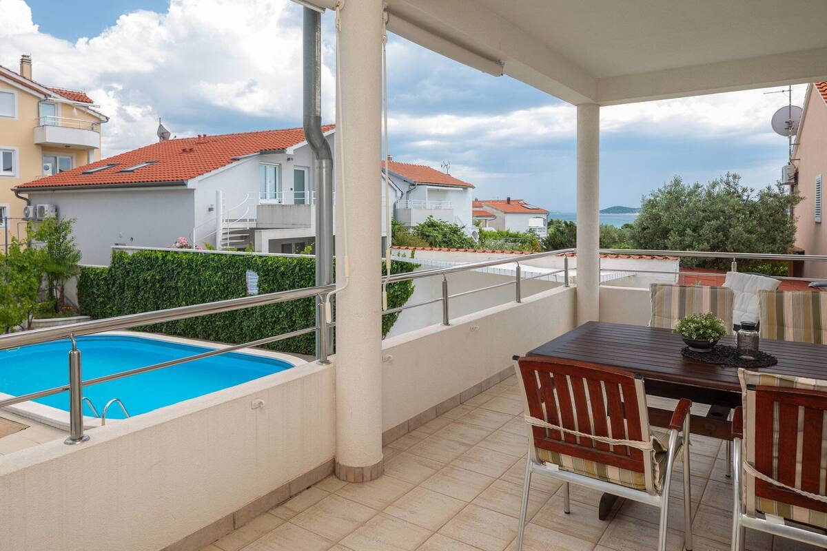 A covered outdoor area with a pool, a table with chairs, and a view of neighboring houses.