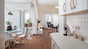 A modern kitchen with white cabinets, a coffee machine, and a dining area with a table and chairs. - Apartments Arausa with Pool (Vodice)