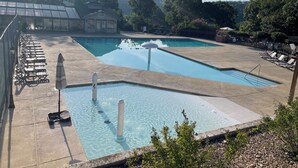 A swimming pool with lounge chairs and umbrellas, surrounded by trees and a building with a glass roof. - GREAT LOCATION LUXURY 3 BDRM 3 BATH LAKEFRONT  HEATED INDOOR POOL STAY&PLAY GOLF (Branson)
