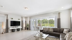 Ein modernes Wohnzimmer mit Flachbildfernseher, Glastisch, Sofa und Blick ins Freie durch große Fenster.