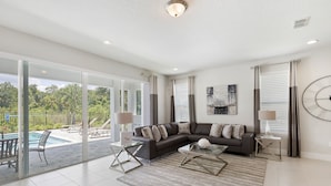 Ein modernes Wohnzimmer mit Ecksofa, Glastisch und Blick auf einen Außenpool.