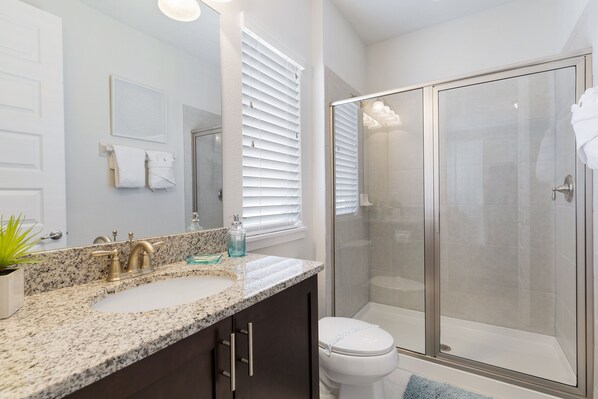 A modern bathroom with a granite countertop, a white sink, a glass shower enclosure, and a toilet.