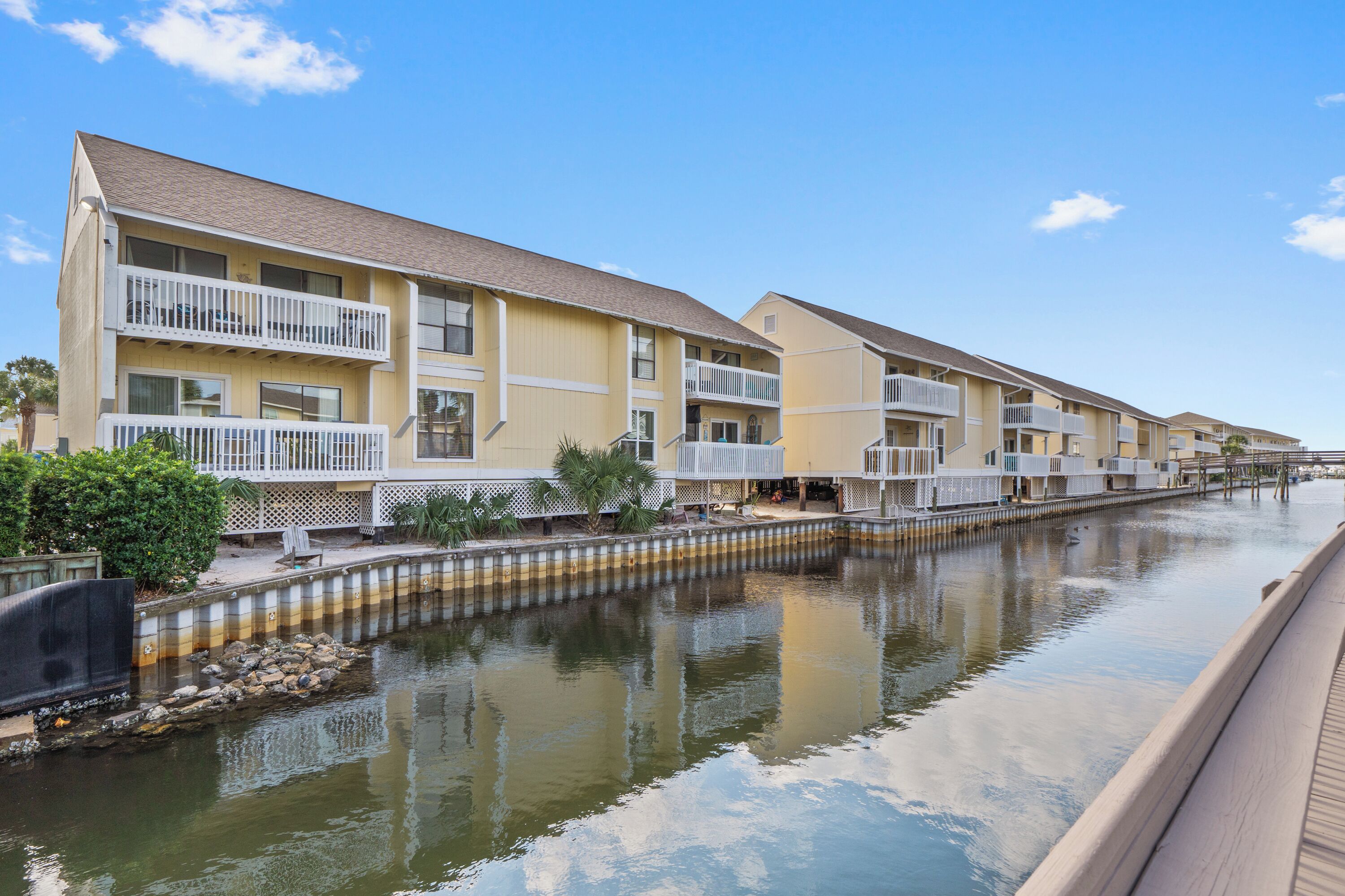 A row of yellow multi-story buildings with balconies, a canal in front, and a wooden boardwalk.
