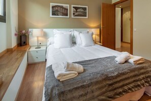 A hotel room with a bed, two bedside tables, a nightstand, a lamp, a wall-mounted picture, and a door. - Charming Old Town Flat Carders with Balcony (Barcelona)