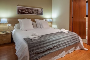 A neatly made bed with white linens, a gray striped blanket, and two white towels. There is a nightstand with a lamp and a book beside the bed. - Charming Old Town Flat Carders with Balcony (Barcelona)
