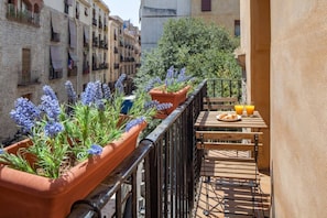 A balcony with terracotta planters containing lavender plants, a wooden table with a plate of croissants and a glass of orange juice, and a view of the cityscape. - Charming Old Town Flat Carders with Balcony (Barcelona)