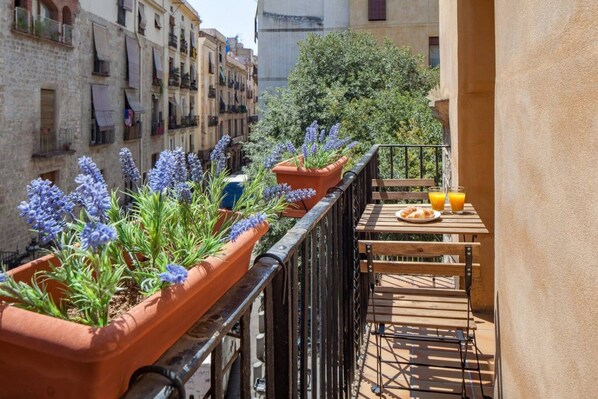 A balcony with terracotta planters containing lavender plants, a wooden table with a plate of croissants and a glass of orange juice, and a view of the cityscape. - Charming Old Town Flat Carders with Balcony (Barcelona)