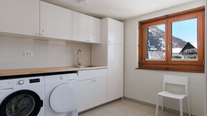 Una cocina compacta con lavadora, un lavabo y una ventana con vistas a casas y montañas.