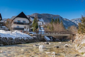 Una casa con un balcone, un ponte di pietra su un fiume e montagne sullo sfondo.