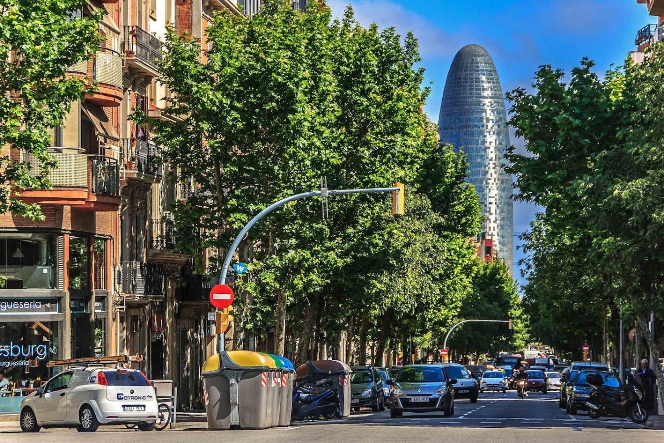 A street scene with a no-entry sign, parked cars, and a tall building in the background.