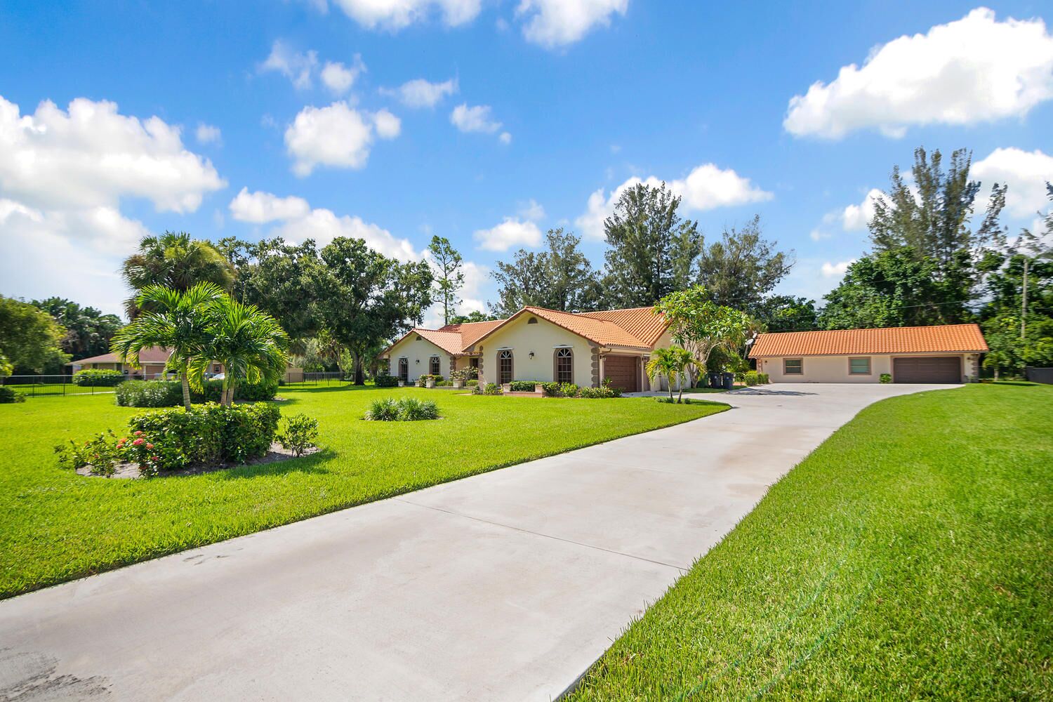 A residential property with a well-maintained lawn, a driveway leading to a house with a red-tiled roof, and a garage.
