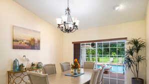 A dining area with a table, chairs, a chandelier, a painting, and a view of a pool. - Spacious pool home in Wellington near WEF (Wellington)