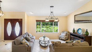 A spacious living room with a sofa set, a coffee table, and a view of a garden through a large window. - Spacious pool home in Wellington near WEF (Wellington)