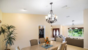 A dining area with a wooden table, chairs, a chandelier, and a potted plant. - Spacious pool home in Wellington near WEF (Wellington)