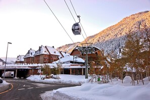 A ski resort with a cable car, snow-covered buildings, and a mountain backdrop.