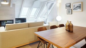 Ett modernt vardagsrum med ett matbord i trä, en beige soffa och en tv.
