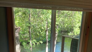 A bedroom with a large window overlooking a forested area and a body of water. - Relaxing cozy cabin on beautiful Pere Marquette River - Recently Renovated!! (Branch)