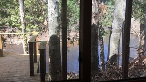 A view through a window with a wooden deck, trees, and a bench. - Relaxing cozy cabin on beautiful Pere Marquette River - Recently Renovated!! (Branch)