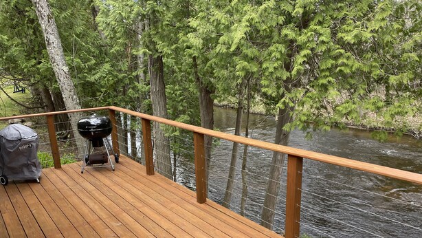 A wooden deck with a grill and a covered grill cart, overlooking a river. - Relaxing cozy cabin on beautiful Pere Marquette River - Recently Renovated!! (Branch)