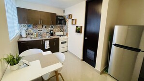 A compact kitchen with a stove, microwave, and refrigerator. There is a dining table with chairs and a small potted plant. - Private Patio Retreat with Zen Vibe and Laundry (Ponce)