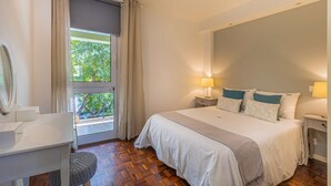 Une chambre à coucher avec un lit, des lampes de chevet, un bureau avec un miroir et une vue sur la verdure à l’extérieur.