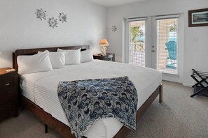 A bedroom with a bed, bedside tables, a lamp, a window with blinds, and a chair.