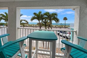 A balcony with a view of the beach and ocean, featuring a table and chairs.