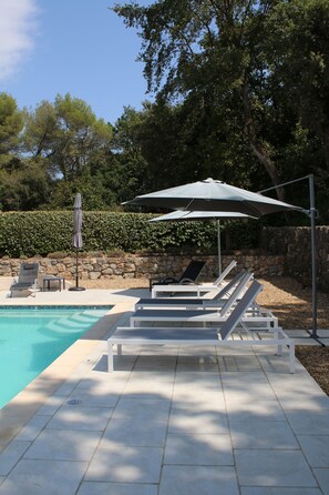 A poolside area with lounge chairs and umbrellas, surrounded by stone walls and trees.