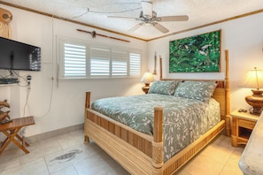 A bedroom with a bed, a television, a window with blinds, a painting, and a ceiling fan. - Condo w/ Private Lanai, Ocean View & On-Site Pool! (Kihei)