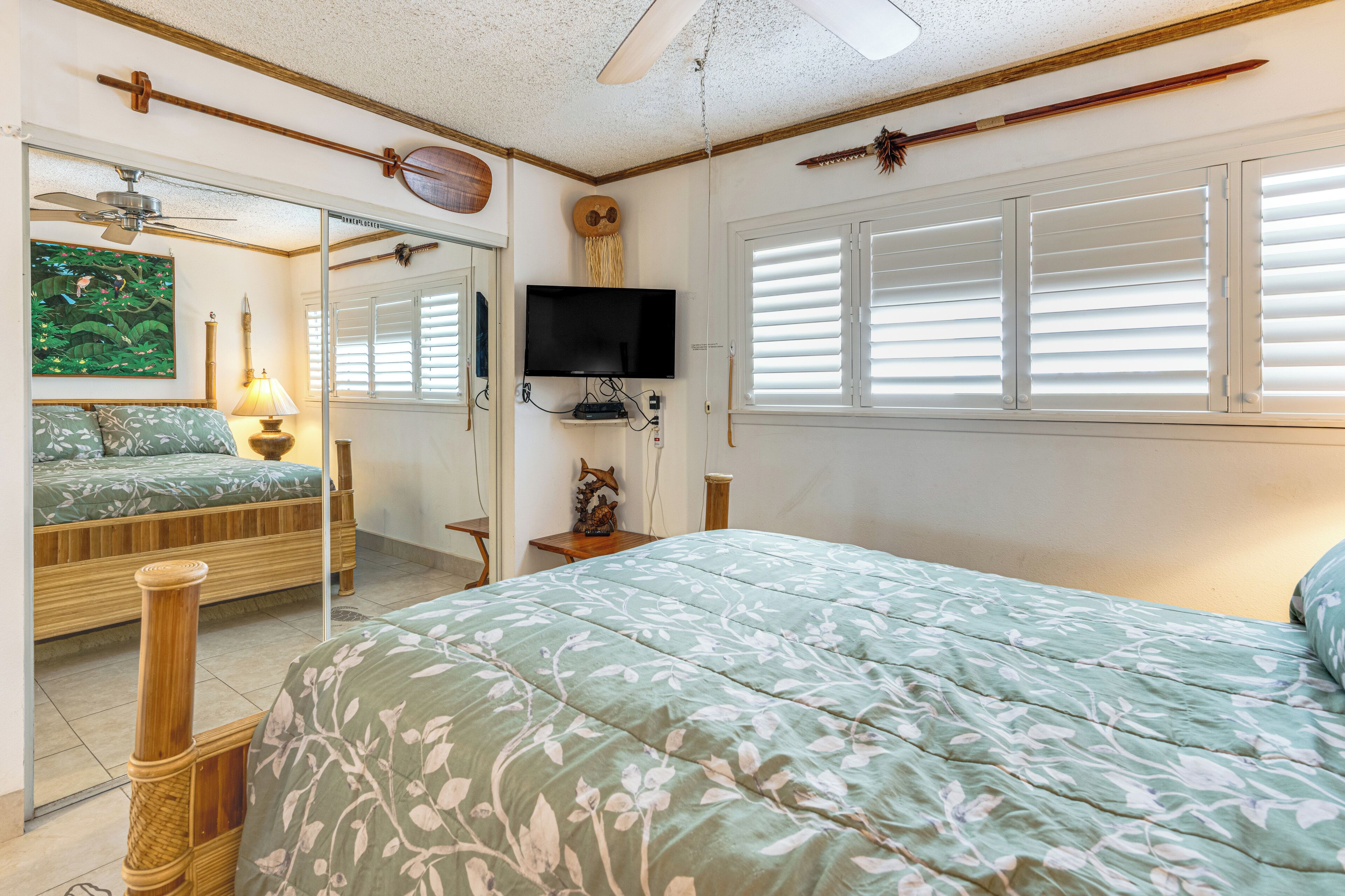 Ein Schlafzimmer mit Bett, Fernseher, Deckenventilator und einem Fenster mit Jalousien.