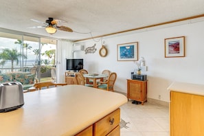A kitchen with a large island, dining area with chairs, a television, and a view of the ocean. - Condo w/ Private Lanai, Ocean View & On-Site Pool! (Kihei)