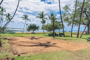 A beach volleyball court with a net, surrounded by palm trees and benches. - Condo w/ Private Lanai, Ocean View & On-Site Pool! (Kihei)