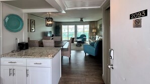 Eine moderne Küche mit Granitarbeitsplatten, ein Essbereich mit gemusterten Stühlen, ein Wohnzimmer mit blauem Sofa und ein Rauchverbot-Schild.