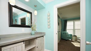 A bathroom with a marble countertop, wooden cabinets, a mirror, and a hanging light fixture. - Sunset Golf Retreat | Cozy 2BR Near Pool & Beach (Destin)