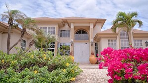 A two-story building with a symmetrical facade, large windows, and a central entrance with a double door. - Aruba Villa Tropical (Noord)