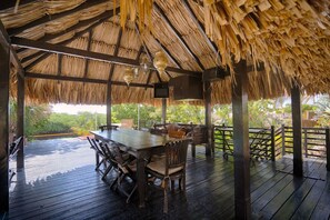 An outdoor wooden deck with a thatched roof, surrounded by lush greenery.